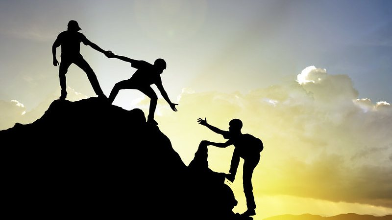 Silhouette of three climbers helping each other with a yellow sky behind them