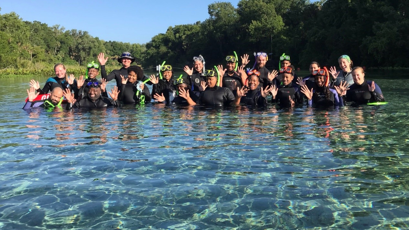A group of people chest-deep in a lake, waving